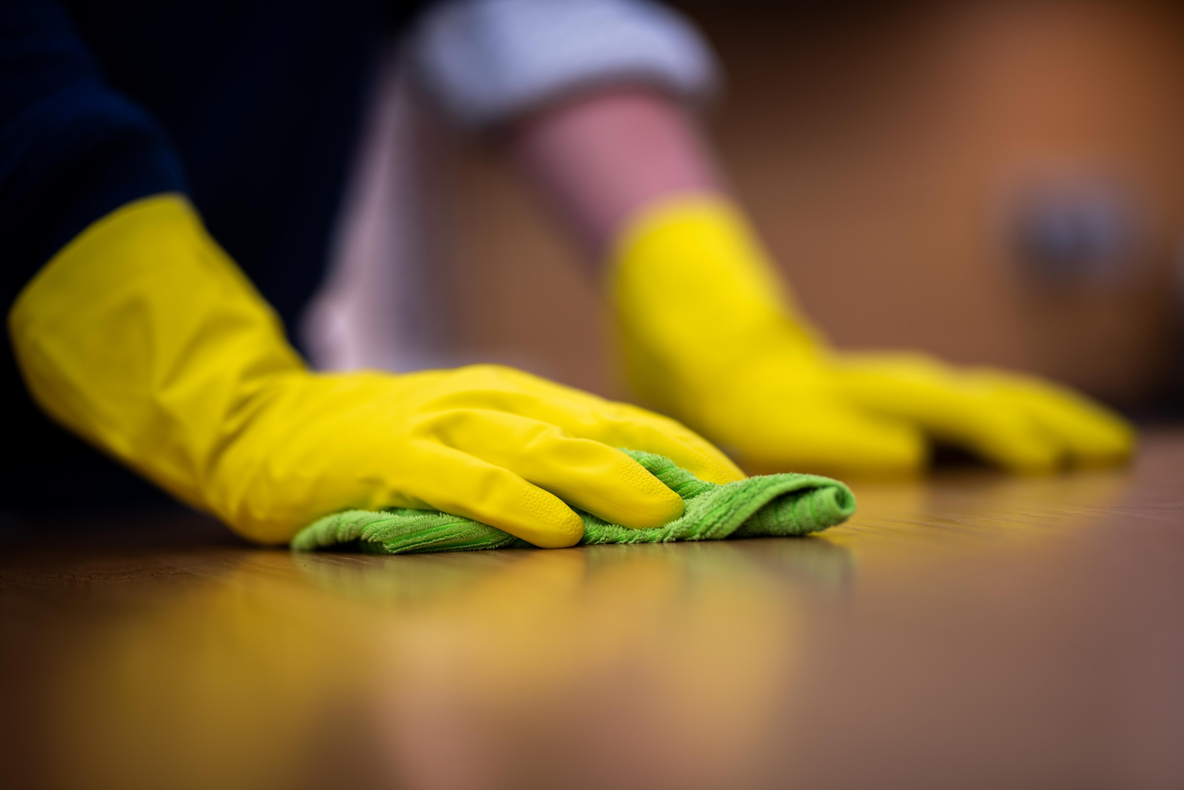 Hände einer Person die mit gelben Gummihandschuhen die Arbeitsplatte putzt. 