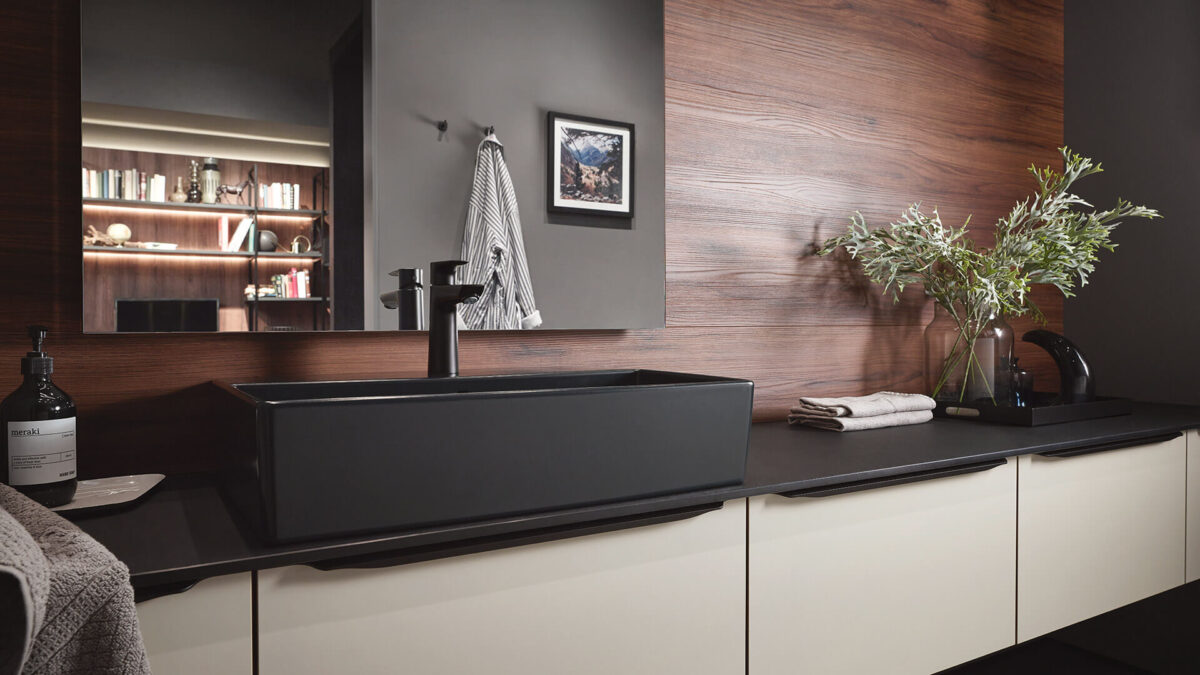 Modernes Badezimmer mit schwarzem Waschbecken, Holzverkleidung und Pflanze auf der Ablage.