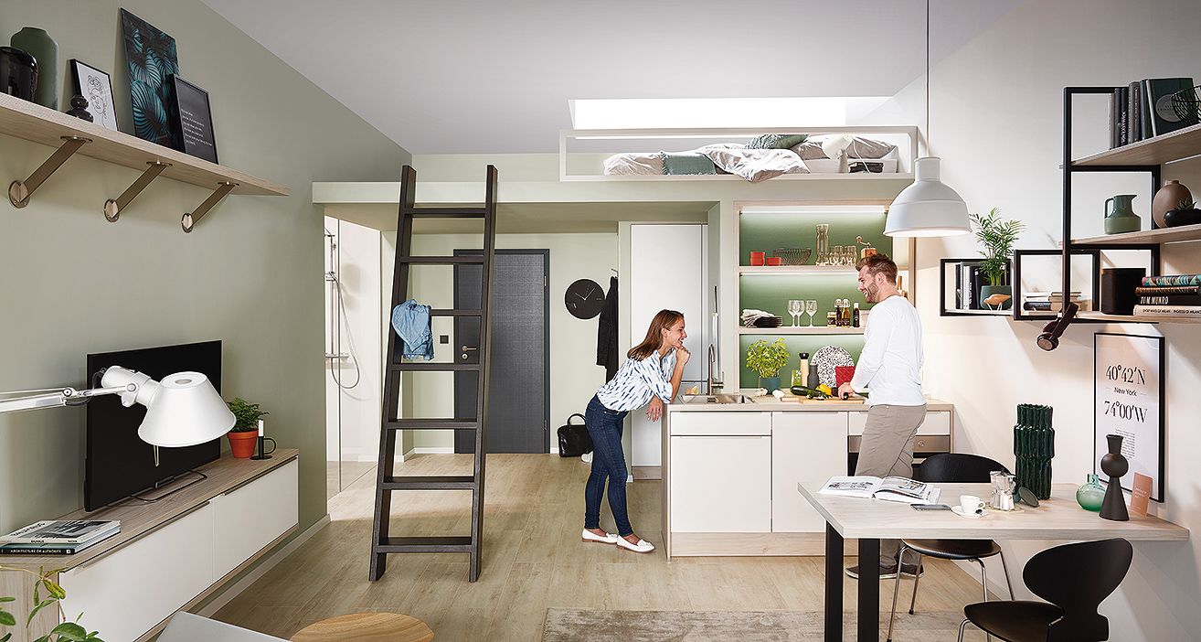 Zwei Menschen unterhalten sich in einer modernen, hellen Einzimmerwohnung mit Küche von Impuls.
