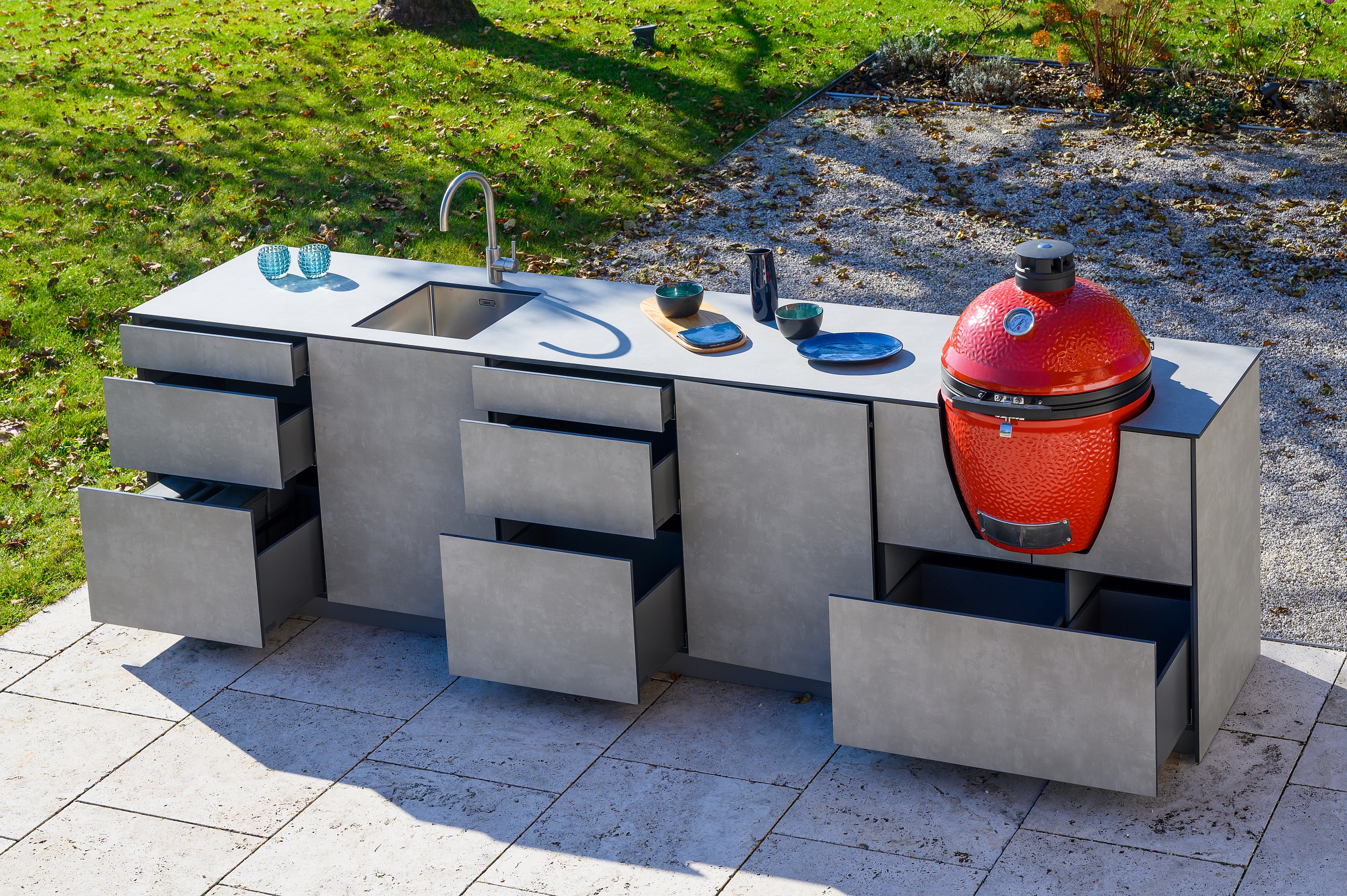 Vogelperspektive auf Küchenzeile auf Terrasse mit rotem Grillei und diversen geöffneten Auszügen