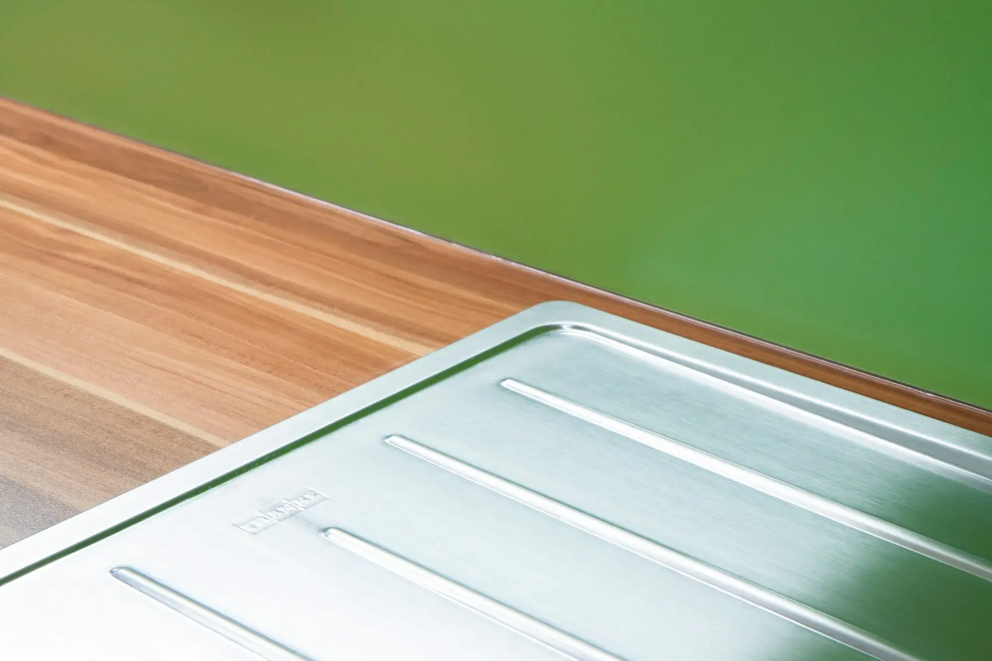 Detailbild Arbeitsplatte in Holz mit Spüle in Edelstahl und Wand in grün.